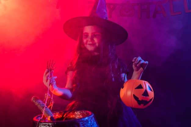 Strega della ragazza del bambino che prepara una pozione nel calderone alle feste di halloween