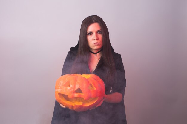 Strega di Halloween che tiene una zucca arancio Jack o Lantern con fumo