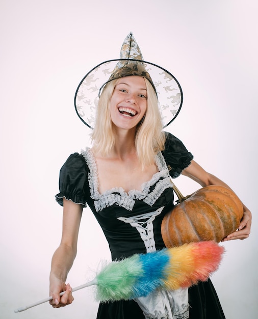 Strega di Halloween con zucca Ampio Halloween party art design Donna sorpresa con cappello da streghe e costume su sfondo bianco Bellezza donna in posa con zucca e cappello di Halloween Party people