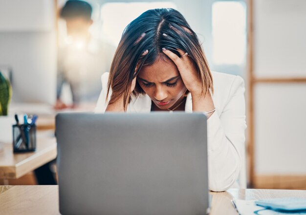 Stress da mal di testa e donna d'affari con esaurimento dovuto a problemi di lavoro su un computer portatile in un ufficio Triste lavoratore aziendale indiano e stanco con ansia mentre lavora su Internet su un computer alla sua scrivania