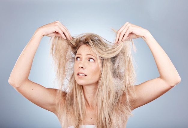 Stress per la cura dei capelli e donna triste per le doppie punte crespo e lo stile disordinato su uno sfondo grigio da studio Modello frustrato infelice e arrabbiato con problemi con i suoi capelli frustrazione e preoccupazione