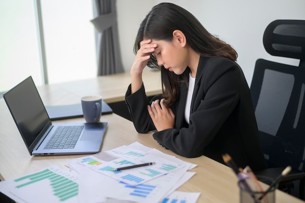 Stressato giovane donna d'affari che lavora al computer portatile con documenti nel moderno concetto di carico di lavoro dell'ufficio