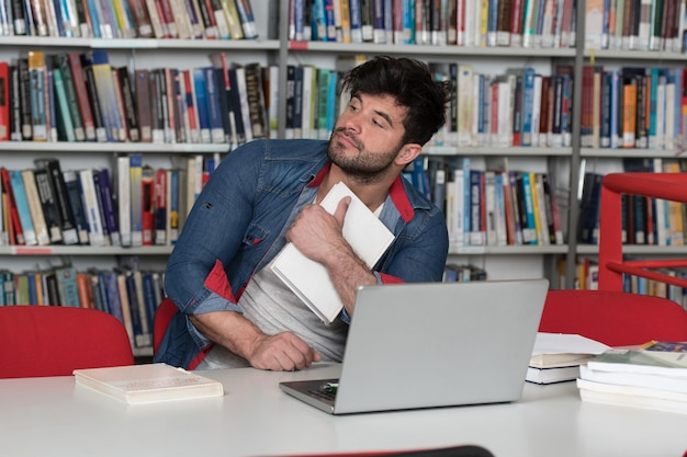 Stressato giovane studente maschio leggendo il libro di testo mentre era seduto in biblioteca