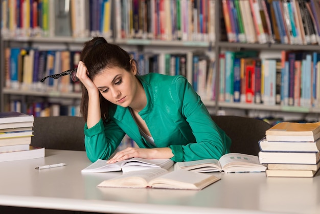 Stressato studente di scuola superiore seduto alla scrivania della biblioteca Profondità di campo