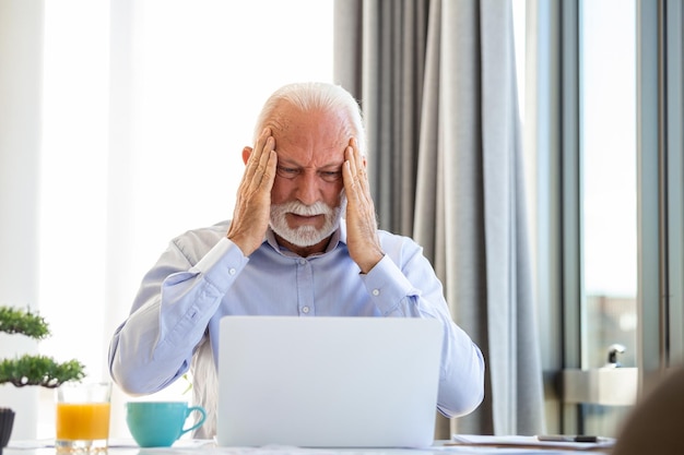 Stressato uomo d'affari maturo con laptop potrebbe anche avere un mal di testa è seduto nella sala riunioni ci sono documenti e laptop sul tavolo spazio di copia