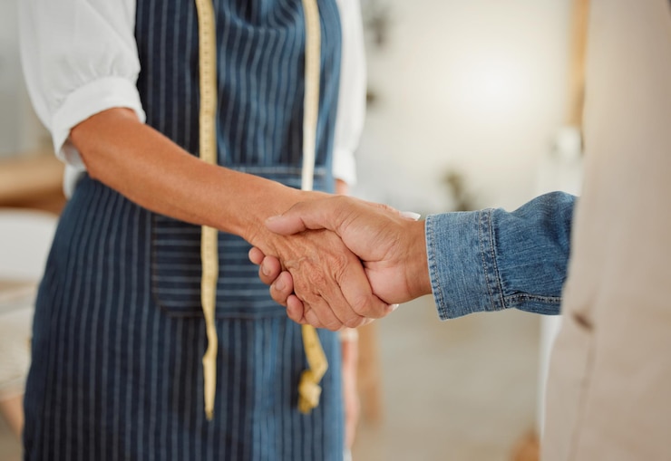 Foto stretta di mano creativa e discussione con il cliente affare e accordo in laboratorio stilista di moda e grembiule sarto che si tiene per mano e persone in affari incontro e collaborazione in studio di progettazione