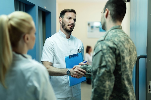 Stretta di mano del soldato dell'esercito con un medico in una hall della clinica Focus è sul medico