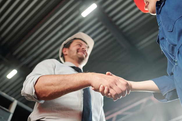 Stretta di mano dell'elegante caposquadra e della sua nuova giovane donna subordinata all'inizio della giornata lavorativa in officina