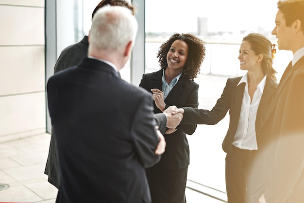 Stretta di mano professionale e gruppo per la negoziazione al lavoro con un sorriso per mostrare sostegno alla collaborazione Uomini d'affari e accordo nella hall per un contratto con successo presso un ufficio aziendale