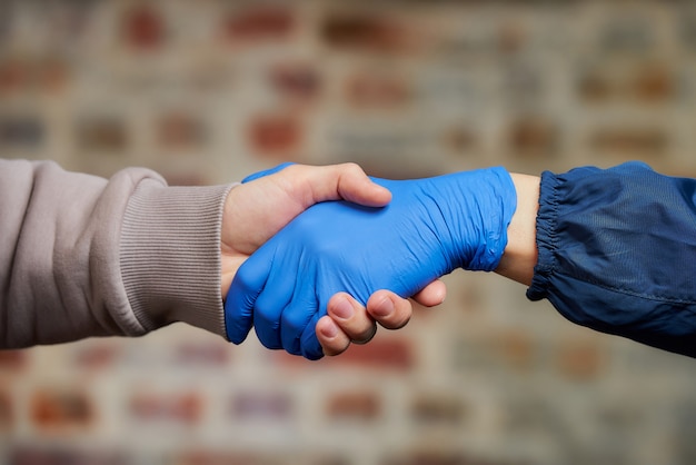 Stretta di mano. Una donna si stringe la mano in guanto medico monouso con un uomo per evitare la diffusione del coronavirus (COVID-19). Due umani si incontrano in una strada.