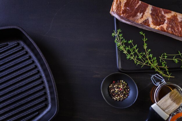 Strisce di pancetta cruda con spezie fresche su un tagliere nero.