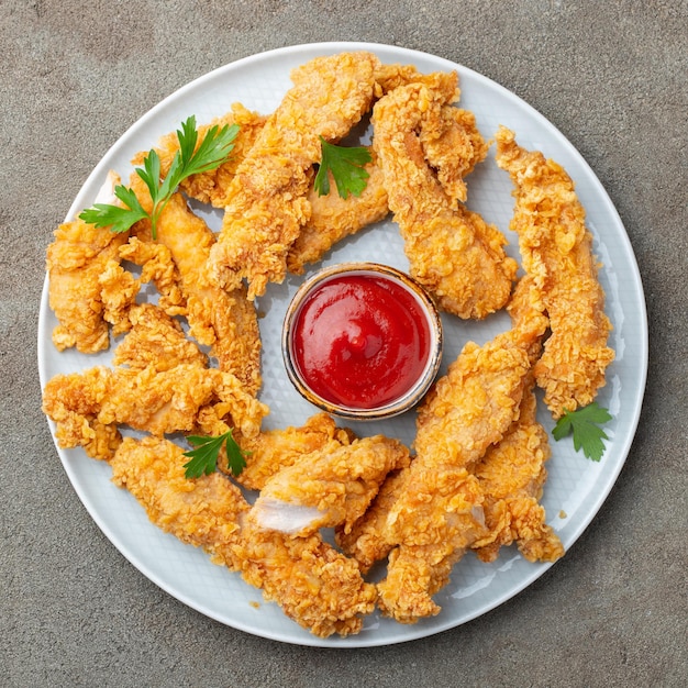 Strisce di pollo al pane con ketchup di pomodoro su un piatto bianco Fast food su sfondo marrone scuro Top view