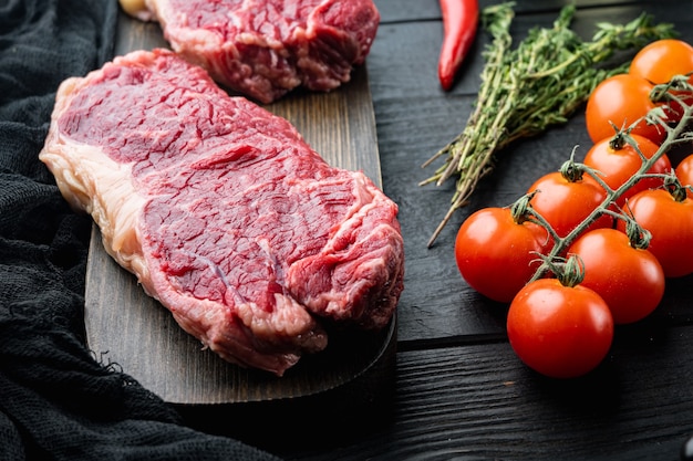 Striscia di bistecca, carne cruda di manzo marmorizzata, sul tavolo di legno nero