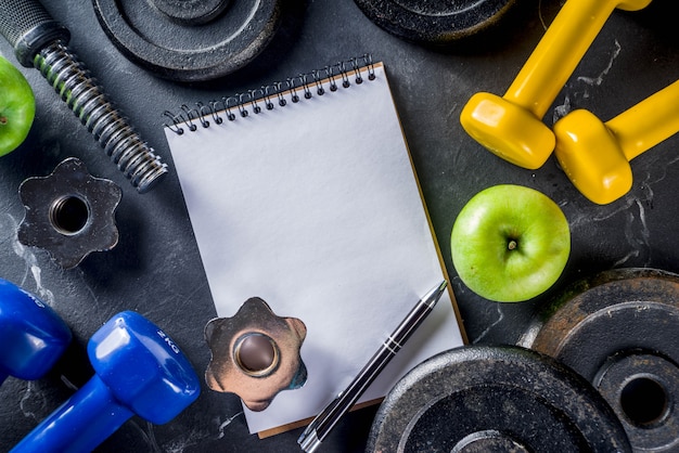 Strumenti di fitness e manubri con il taccuino in bianco