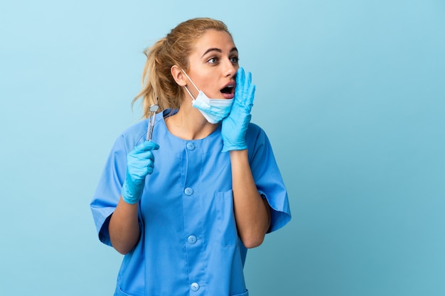 Strumenti di tenuta del dentista della giovane donna sopra gridare blu isolato con la bocca spalancata