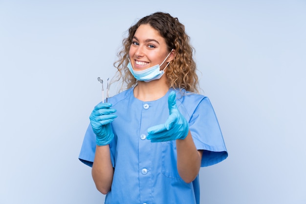 Strumenti di tenuta del giovane dentista biondo della donna sul handshake blu della parete dopo il buon affare