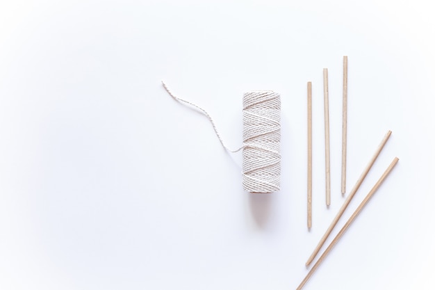 Strumenti e materiali per la tessitura di macramè, una bobina con corda bianca e bastoncini sbiancati