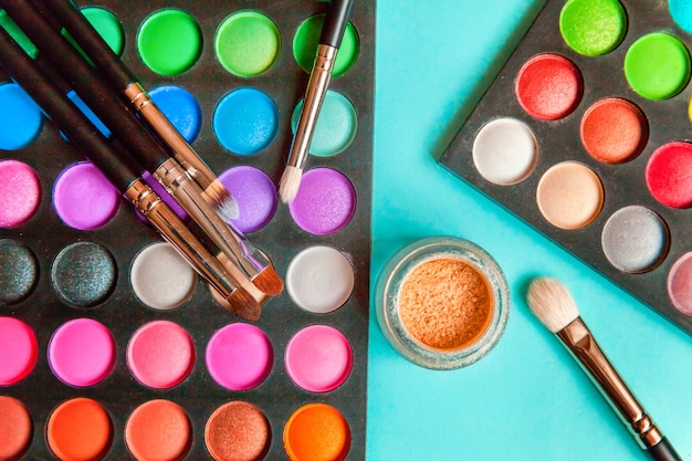 Strumenti per trucco e cosmetici diverse tonalità di palette di ombretti e pennello per il trucco sul tavolo pastello blu colorato alla moda. Vista dall'alto laici piatta