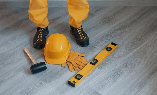 Strumenti sul pavimento Tuttofare in uniforme gialla in piedi all'interno Concezione di ristrutturazione della casa