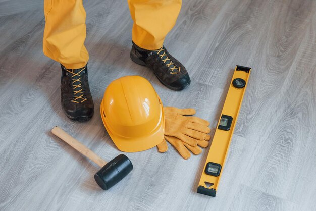 Strumenti sul pavimento Tuttofare in uniforme gialla in piedi all'interno Concezione di ristrutturazione della casa