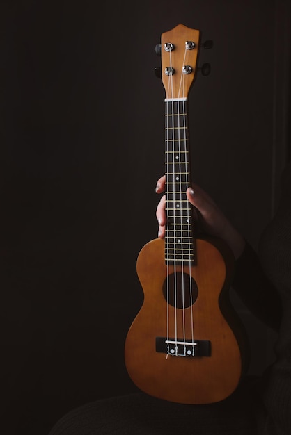 Strumento musicale ukulele in mano di una donna su uno sfondo scuro