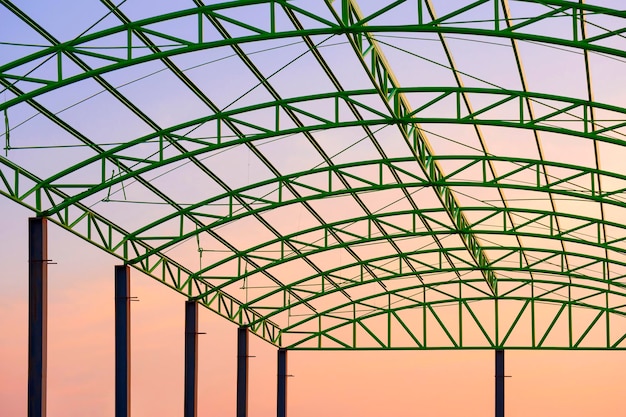 Struttura del tetto in metallo verde di un edificio industriale in cantiere sullo sfondo del cielo al tramonto