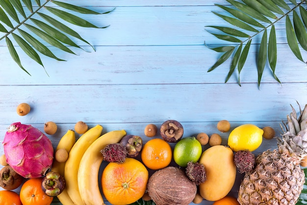 Struttura di frutti tropicali dell&#39;arcobaleno sano con foglie di palma sulla tavola di legno blu