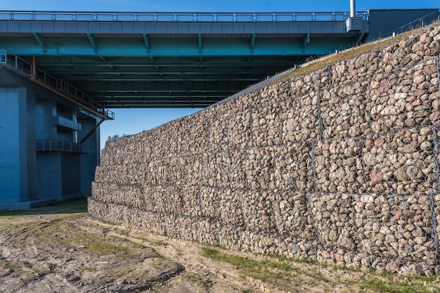 Struttura ingegneristica realizzata con pietre dietro una rete metallica per rafforzare la sponda del fiume vicino al ponte stradale