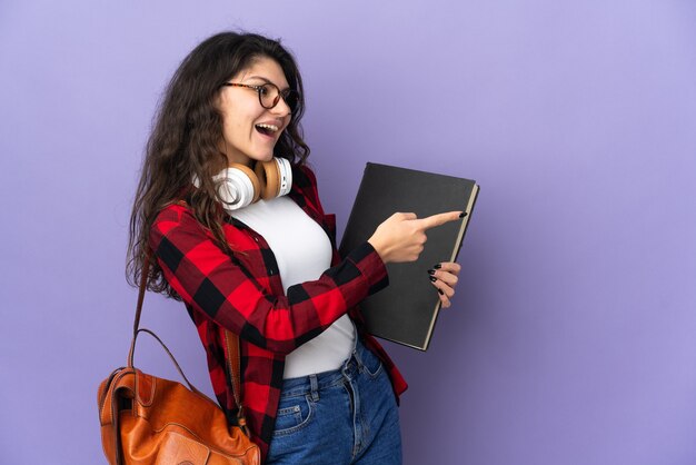 Studente adolescente isolato su sfondo viola che punta il dito di lato e presenta un prodotto