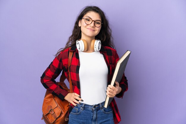 Studente adolescente isolato sulla parete viola in posa con le braccia all'anca e sorridente