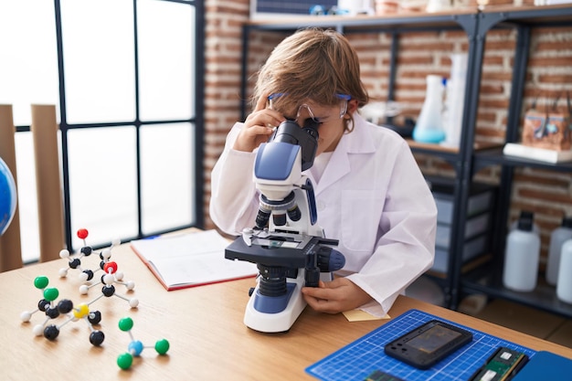 Studente adorabile del ragazzo caucasico che utilizza il microscopio all'aula