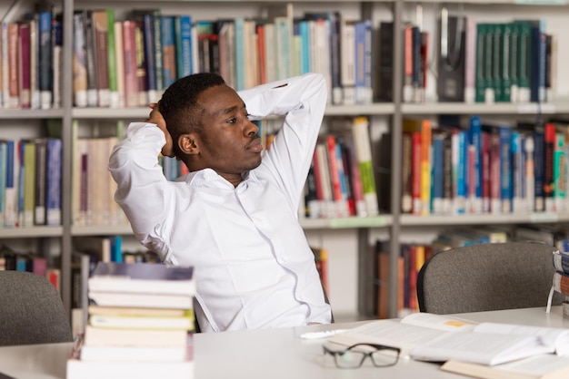 Studente africano stressato di scuola superiore seduto alla scrivania della biblioteca Profondità di campo ridotta