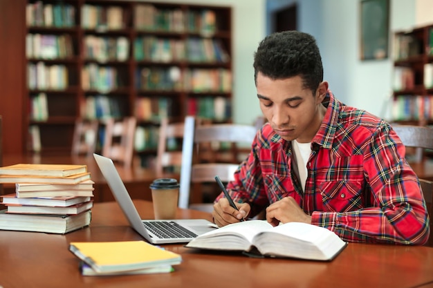 Studente afroamericano con laptop che studia in biblioteca