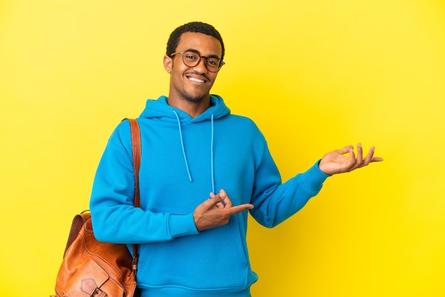 Studente afroamericano su sfondo giallo isolato che estende le mani di lato per invitare a venire