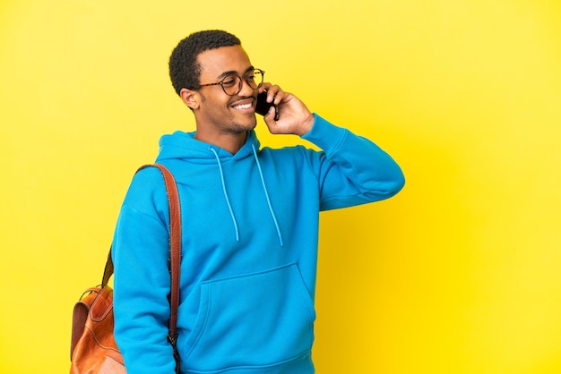 Studente afroamericano su sfondo giallo isolato mantenendo una conversazione con il telefono cellulare