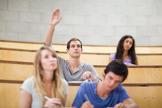 Studente alza la mano mentre i suoi compagni di classe prendono appunti