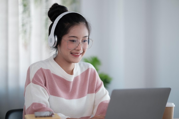 Studente asiatica che indossa le cuffie che parla in chat online che si incontra usando un portatile nel campus universitario o in un ufficio virtuale Studente universitaria di sesso femminile che impara a distanza