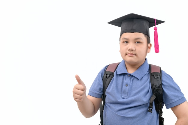 Studente asiatico intelligente indossare il cappello di laurea e mostrando il pollice in su e guardando la telecamera isolata su bianco