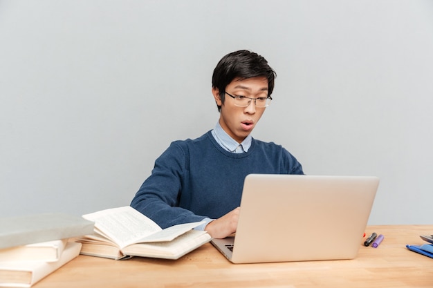 Studente asiatico si siede al tavolo. sorpreso