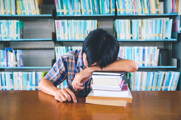 Studente asiatico stanco che dorme allo scrittorio in una biblioteca