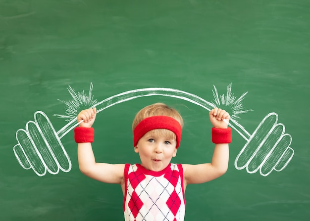 Studente bambino divertente in classe contro la lavagna verde. Educazione fisica.