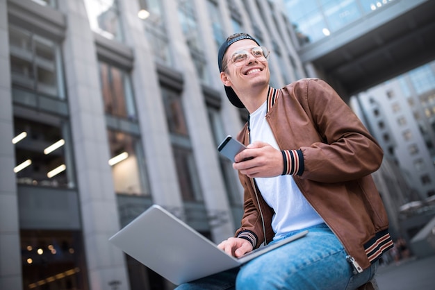 Studente bello felice che guarda lo schermo del computer mentre digita qualcosa sulla tastiera del laptop