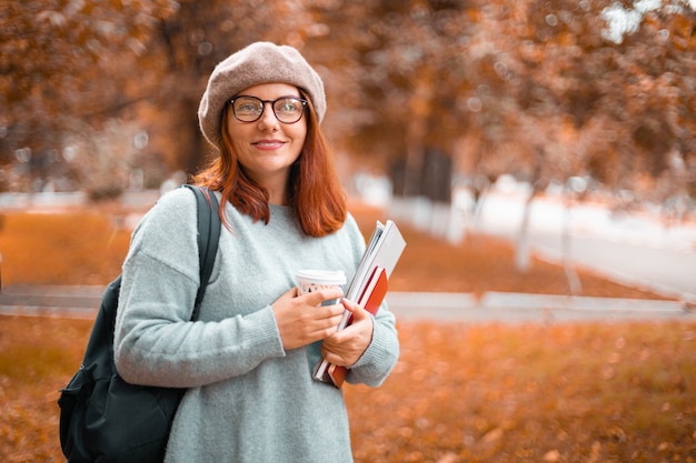 Studente carino che cammina nel parco indossando abiti casual con occhiali che tengono quaderni e libri nel parco...