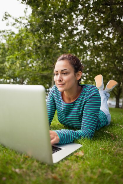 Studente casuale che si trova sull&#39;erba facendo uso del computer portatile