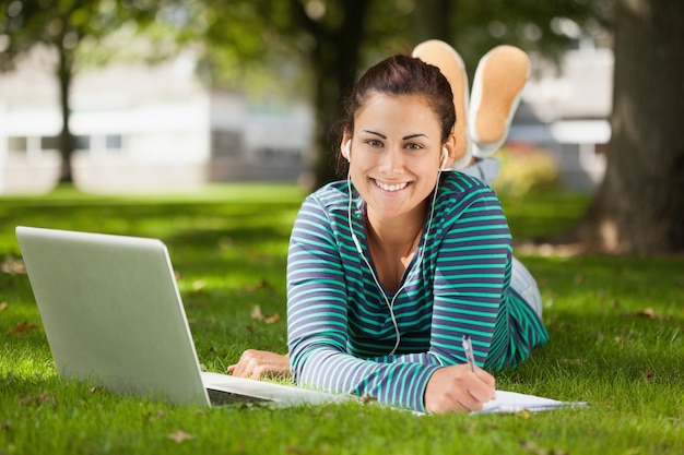 Studente casuale felice che si trova sull&#39;erba che cattura le note