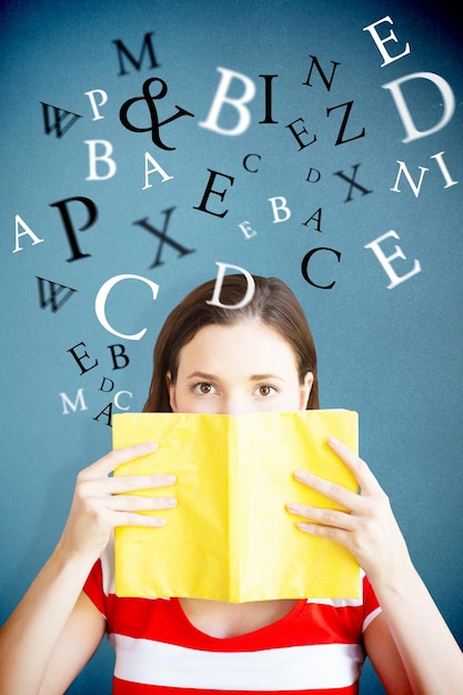 Studente che copre il viso con il libro in libreria su sfondo blu