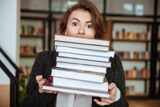 Studente che guarda dalla pila di libro mentre stando nella biblioteca