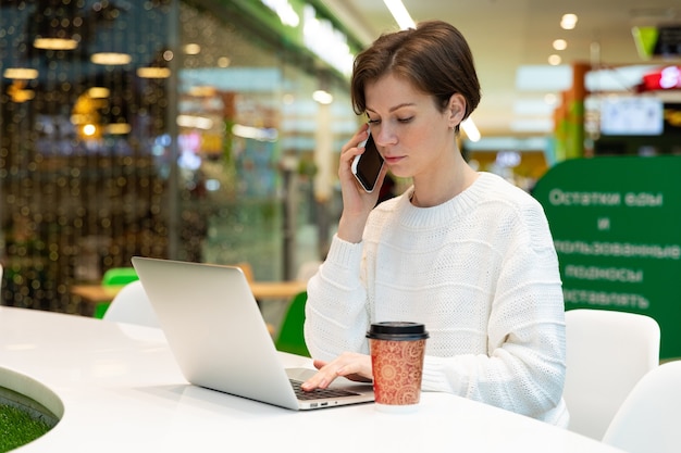 Studente che lavora a un laptop in un bar in un centro commerciale, concetto di lavoro autonomo e lavoro a distanza