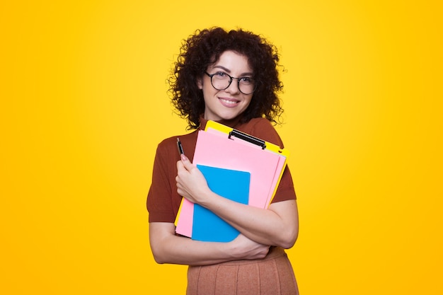 Studente con i capelli ricci che tiene le cartelle su sfondo giallo ritratto elegante per il design educativo