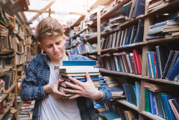 Studente con molti libri nelle mani di una vecchia biblioteca d'atmosfera.